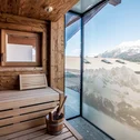 Sauna mit Holzbank und Blick auf schneebedeckte Berge durch Glasfenster