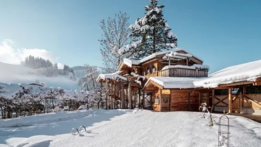 Verschneites Holzhaus in sonniger Winterlandschaft mit blauem Himmel