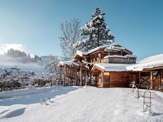 Verschneites Holzhaus in sonniger Winterlandschaft mit blauem Himmel