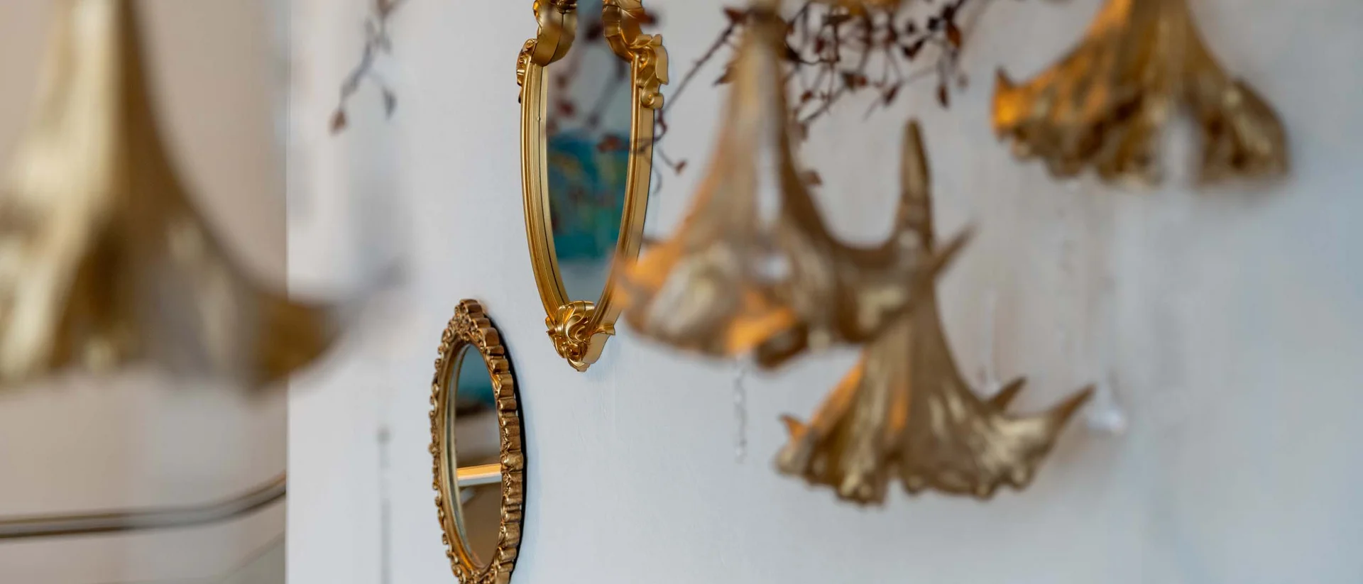 Goldene Spiegel und dekorative Anhänger an einer weißen Wand
