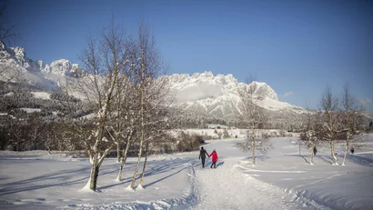 Paar spaziert im Schnee vor verschneiten Bergen bei klarem Himmel