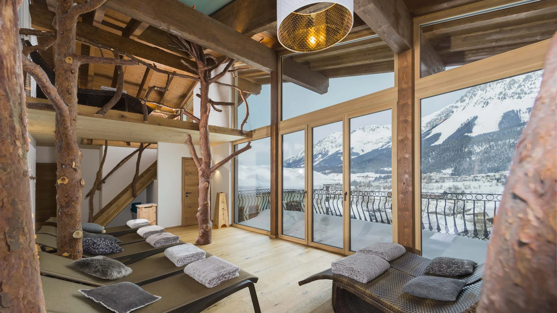 Ruheraum mit Liegen, Holzdeko und Alpenblick durch große Fenster