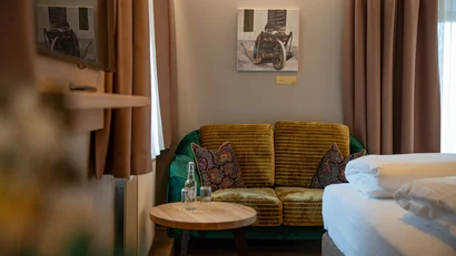 Gemütliches Zimmer mit grünem Sofa, kleinem Tisch und Porträt an der Wand