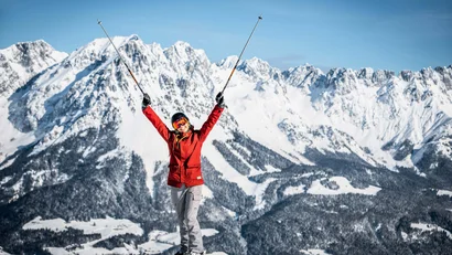 Fröhlicher Skifahrer mit Skistöcken vor schneebedeckten Bergen