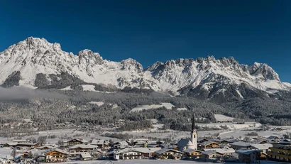 Schneebedeckte Alpen mit Dorf und Kirche im Vordergrund unter klarem Himmel