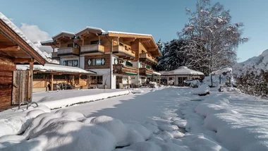 Schneebedecktes Chalet mit Garten und Bäumen an einem sonnigen Wintertag