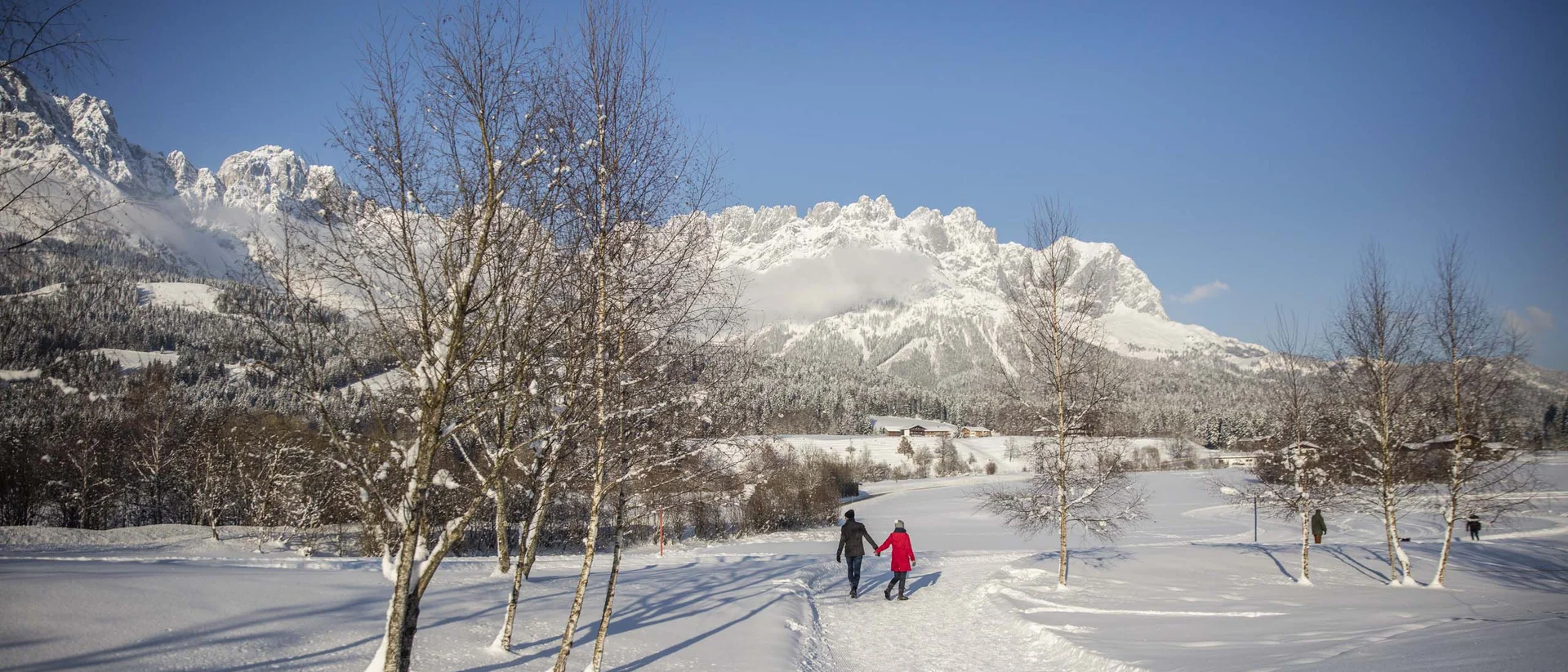 Paar spaziert auf verschneitem Weg mit Bergen im Hintergrund