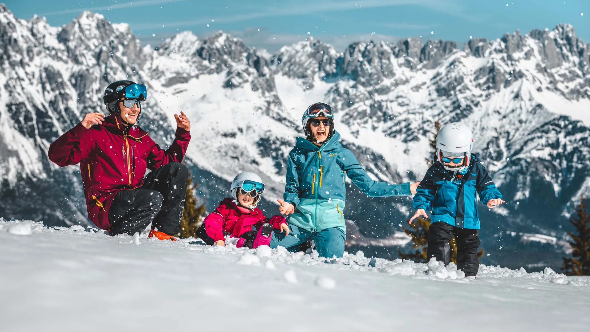 Familie spielt lachend im Schnee vor schneebedeckten Bergen