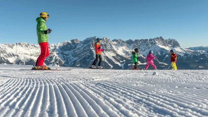 Skilehrer mit Kindern beim Skifahren vor Bergpanorama